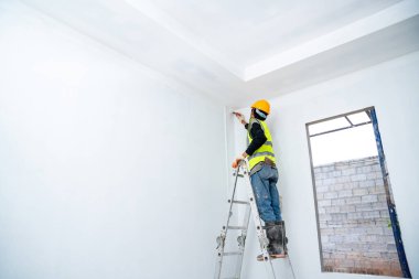 Boya fırçası ve kovayla tamamlanmamış bir binanın duvarını boyayan ressam inşaat alanındaki merdivenle büyük boş bir alanda izole edilmiş.