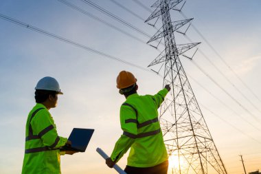 Elektrik santralinde mühendisler ve teknisyenler gün batımında yüksek voltajlı elektrik iletim kulesi üreterek planlama çalışmalarını görmek için çalışıyor.