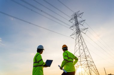Elektrik santralinde çalışan mühendisler ve teknisyenlerin ekip çalışması planlama çalışmalarını gün batımında yüksek voltajlı elektrik iletim kulesi üreterek görmek için