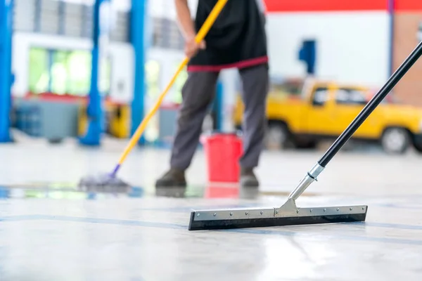 Boş bir depo veya araba servisi merkezinde, yeni epoksi katının koruyucu giysilerini temizlerken üniforma içindeki suyu temizlemek için paspas kullanan odak paspası, servis elemanını seçin.