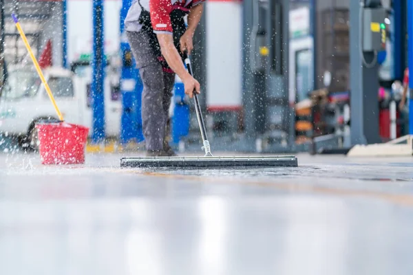 Servis elemanı üniforma içindeki suyu temizlemek için paspas kullanıyor. Boş bir depoda ya da araba hizmet merkezinde yeni epoksi katının koruyucu giysilerini temizliyor..