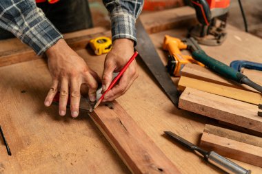 Erkek marangozun eli, inşaat alanındaki bir tahta parçasına kalem kullanıyor.