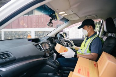 Kredi kartı okuyucu kullanan bir kurye. Deponun dışında paketlerle birlikte minibüsün içinde. Kargo