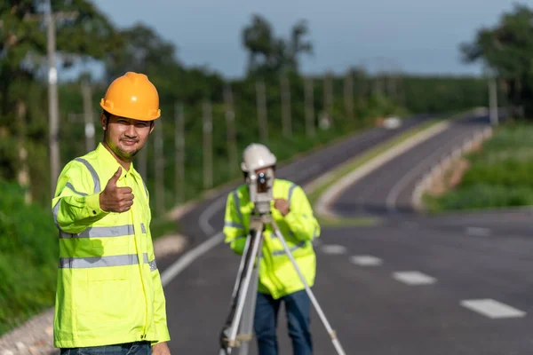 道路建設現場のカメラを見てデジタルレベルを持つアジアの幸せな測量技術者 土木技術者 測量機器 — ストック写真
