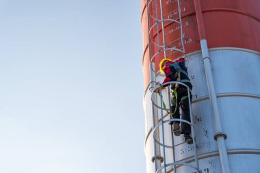 Endüstriyel yükseklik ve güvenliği vurgulayarak yüksek beton silonun sabit merdivenine tırmanan bir işçi..