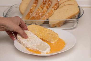Woman hand passing bread through egg and flour (Torrijas). Typical Spanish Easter sweet. Traditional home cooking concept. Horizontal photography, close-up and selective focus