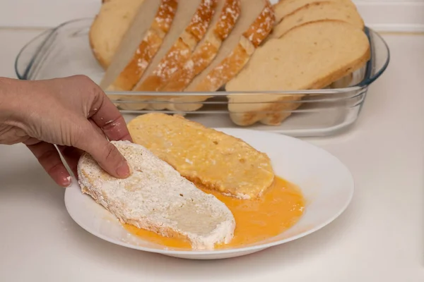 Woman hand passing bread through egg and flour (Torrijas). Typical Spanish Easter sweet. Traditional home cooking concept. Horizontal photography, close-up and selective focus