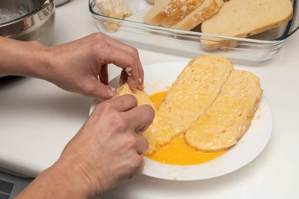 Woman's hands passing bread through egg and flour (Torrijas). Typical Spanish Easter sweet. Traditional home cooking concept. Horizontal photography, close-up and selective focus