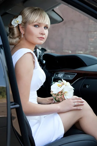 Portret van een mooie bruid in een auto met een boeket van bloemen. — Stockfoto