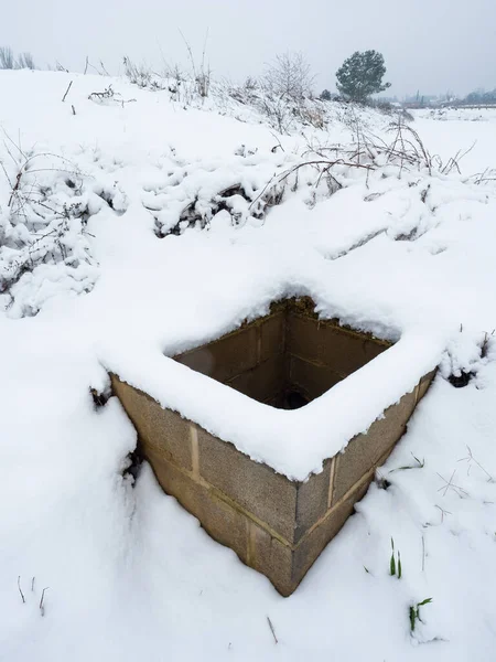 Ön planda bir kuyu olan çok karlı bir manzara.