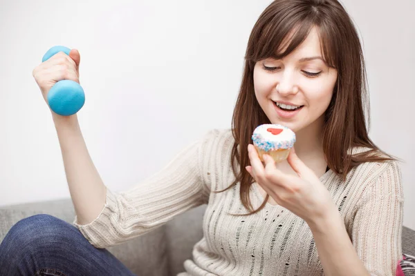 Woman exercising on sofa with cupcake in hand — Stock Photo, Image