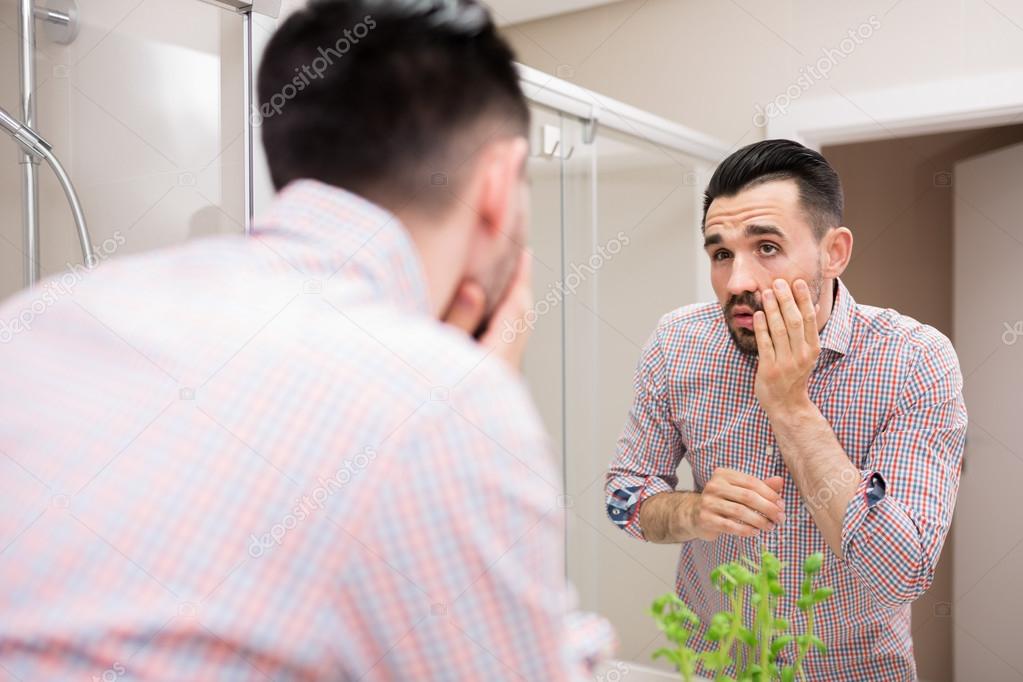 Man in bathroom mirror looking at his face