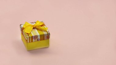 Pembe arka planda sarı fiyonklu bir kutuda hediye.