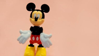 Miki Fare arka planda duruyor ve elleriyle farklı işaretler gösteriyor.