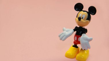 Miki Fare arka planda duruyor ve elleriyle farklı işaretler gösteriyor.