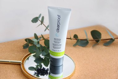 Mary Kay şirketinin tüpündeki sıvı kömür maskesi ahşap bir masanın üzerinde, yanında da 15.03.2021 beyaz arka planda bir okaliptüs dalı var.