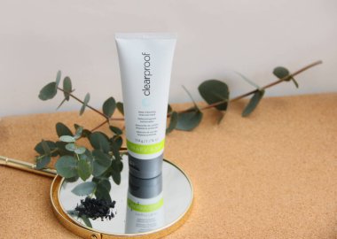 Mary Kay şirketinin tüpündeki sıvı kömür maskesi ahşap bir masanın üzerinde, yanında da 15.03.2021 beyaz arka planda bir okaliptüs dalı var.