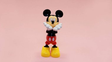 Mickey Mouse pembe bir arka planda duruyor ve elleri ağzına kadar havada öpüşüyor. Yüksek kalite fotoğraf