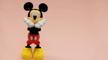 Mickey Mouse pembe bir arka planda duruyor ve elleri ağzına kadar havada öpüşüyor. Yüksek kalite fotoğraf