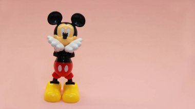 Mickey Mouse pembe bir arka planda duruyor ve elleri ağzına kadar havada öpüşüyor. Yüksek kalite fotoğraf