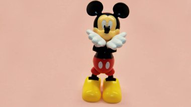 Mickey Mouse pembe bir arka planda duruyor ve elleri ağzına kadar havada öpüşüyor. Yüksek kalite fotoğraf