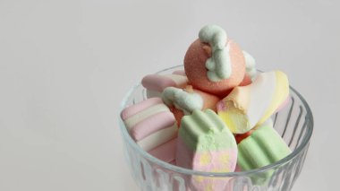 Beyaz arka planda cam bir vazoda şekerleme. Vazodaki farklı şekillerde şekerlemeler. Şekerler.