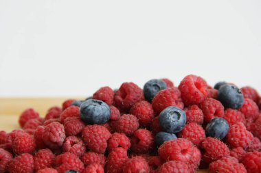 Beyaz arka planda taze ahududu ve yaban mersini. Yaban mersini ve ahududu ağaçtan bir arka planda.