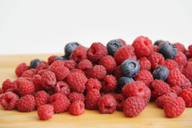 Beyaz arka planda taze ahududu ve yaban mersini. Yaban mersini ve ahududu ağaçtan bir arka planda.