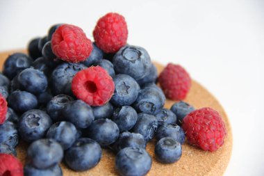 Beyaz arka planda taze ahududu ve yaban mersini. Yaban mersini ve ahududu ağaçtan bir arka planda.