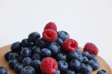 Beyaz arka planda taze ahududu ve yaban mersini. Yaban mersini ve ahududu ağaçtan bir arka planda.