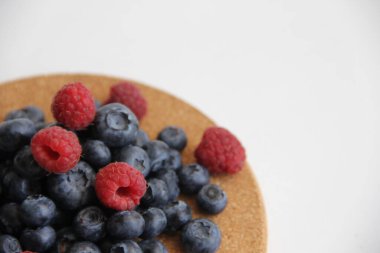 Beyaz arka planda taze ahududu ve yaban mersini. Yaban mersini ve ahududu ağaçtan bir arka planda.