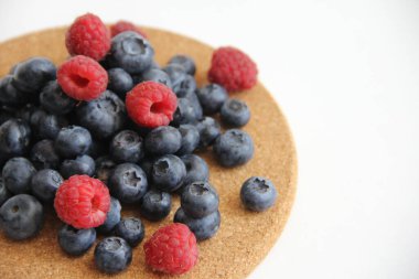 Beyaz arka planda taze ahududu ve yaban mersini. Yaban mersini ve ahududu ağaçtan bir arka planda.