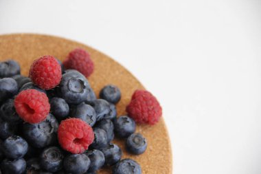 Beyaz arka planda taze ahududu ve yaban mersini. Yaban mersini ve ahududu ağaçtan bir arka planda.