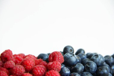 Beyaz arka planda taze ahududu ve yaban mersini. Yaban mersini ve ahududu ağaçtan bir arka planda.