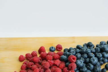 Beyaz arka planda taze ahududu ve yaban mersini. Yaban mersini ve ahududu ağaçtan bir arka planda.