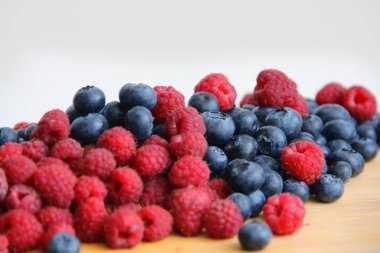 Beyaz arka planda taze ahududu ve yaban mersini. Yaban mersini ve ahududu ağaçtan bir arka planda.