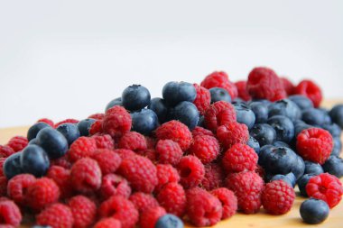 Beyaz arka planda taze ahududu ve yaban mersini. Yaban mersini ve ahududu ağaçtan bir arka planda.