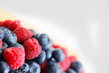 Beyaz arka planda taze ahududu ve yaban mersini. Yaban mersini ve ahududu ağaçtan bir arka planda.