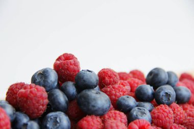 Beyaz arka planda taze ahududu ve yaban mersini. Yaban mersini ve ahududu ağaçtan bir arka planda.