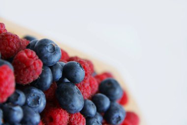 Beyaz arka planda taze ahududu ve yaban mersini. Yaban mersini ve ahududu ağaçtan bir arka planda.