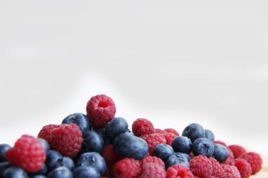 Beyaz arka planda taze ahududu ve yaban mersini. Yaban mersini ve ahududu ağaçtan bir arka planda.