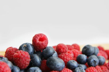 Beyaz arka planda taze ahududu ve yaban mersini. Yaban mersini ve ahududu ağaçtan bir arka planda.