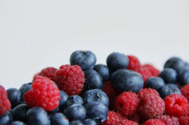 Beyaz arka planda taze ahududu ve yaban mersini. Yaban mersini ve ahududu ağaçtan bir arka planda.