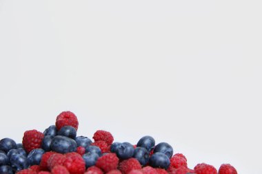 Beyaz arka planda taze ahududu ve yaban mersini. Yaban mersini ve ahududu ağaçtan bir arka planda.