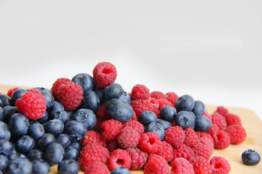 Beyaz arka planda taze ahududu ve yaban mersini. Yaban mersini ve ahududu ağaçtan bir arka planda.