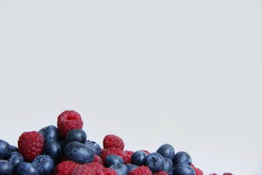 Beyaz arka planda taze ahududu ve yaban mersini. Yaban mersini ve ahududu ağaçtan bir arka planda.