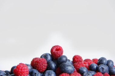 Beyaz arka planda taze ahududu ve yaban mersini. Yaban mersini ve ahududu ağaçtan bir arka planda.