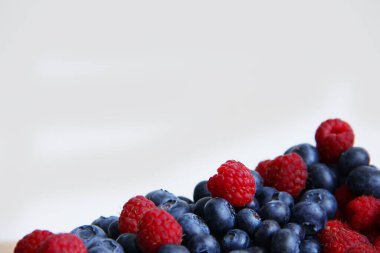 Beyaz arka planda taze ahududu ve yaban mersini. Yaban mersini ve ahududu ağaçtan bir arka planda.