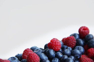 Beyaz arka planda taze ahududu ve yaban mersini. Yaban mersini ve ahududu ağaçtan bir arka planda.