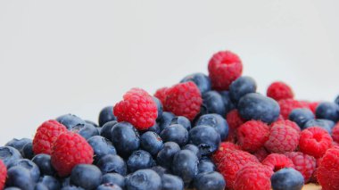 Beyaz arka planda taze ahududu ve yaban mersini. Yaban mersini ve ahududu ağaçtan bir arka planda.